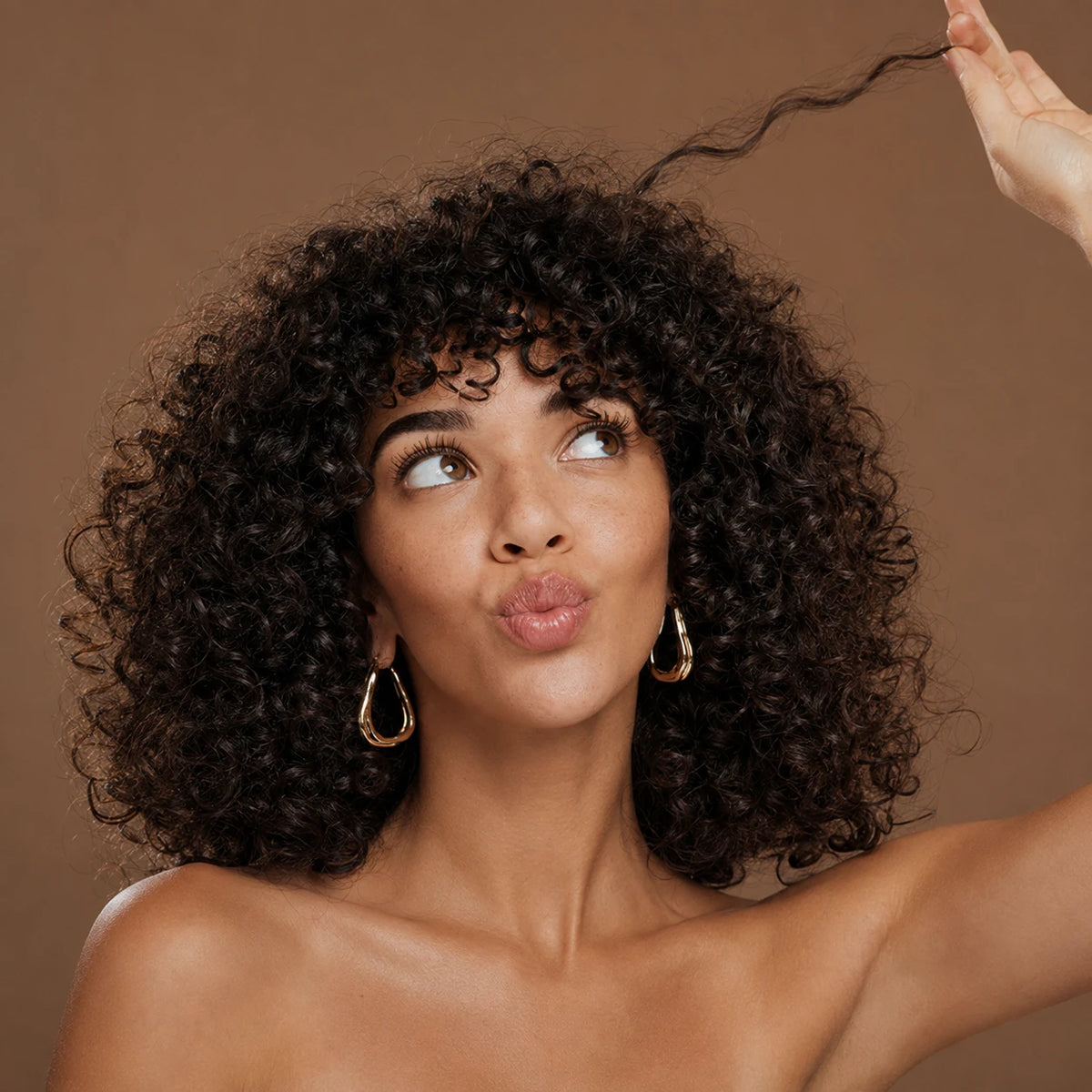 Woman with voluminous curly black hair lifting one curl against a warm brown background.